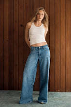 Model wearing the Soho Vintage mid-blue wide-leg jeans with a fitted white tank, showing the mid-rise waist, relaxed seat and full-length loose-leg silhouette in a lifestyle front view.