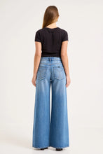Model wearing the mid-blue jeans with a fitted black tee, showing the square back pockets, back yoke and relaxed wide-leg silhouette in a full-length back view.
