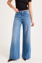 Close-up of the mid-blue jeans worn with a black tee, showing the waistband, silver button, zip fly, front scoop pockets, belt loops and subtle vintage wash detailing.