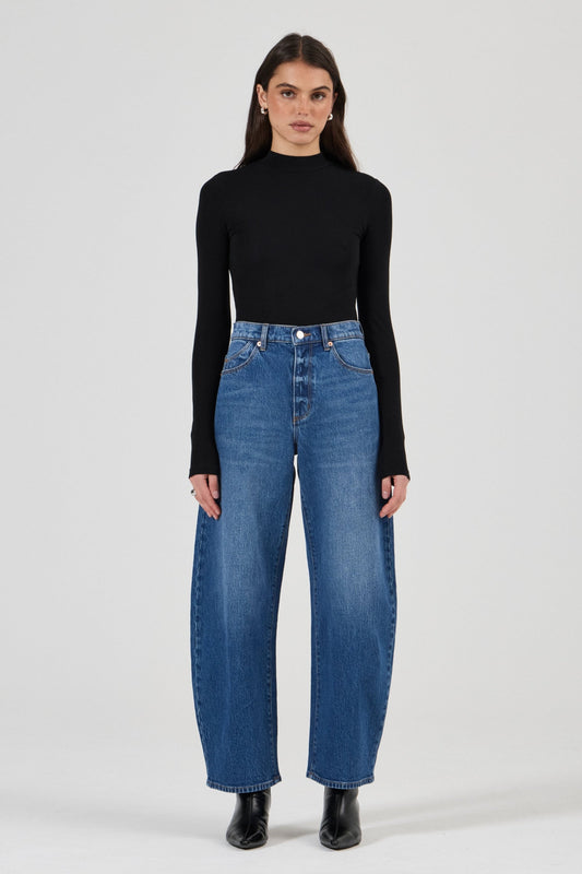 Model wearing the Rolla's Gigi Barrel Jean in Reign with a black turtleneck top, showing the super high-rise sculptural barrel-leg fit, full-length front view