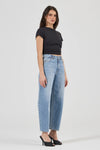 Model wearing light blue high-rise barrel jeans with a fitted black short-sleeve tee and black open-toe heels, showing the front pocket placement, relaxed curved leg silhouette and cropped hems.