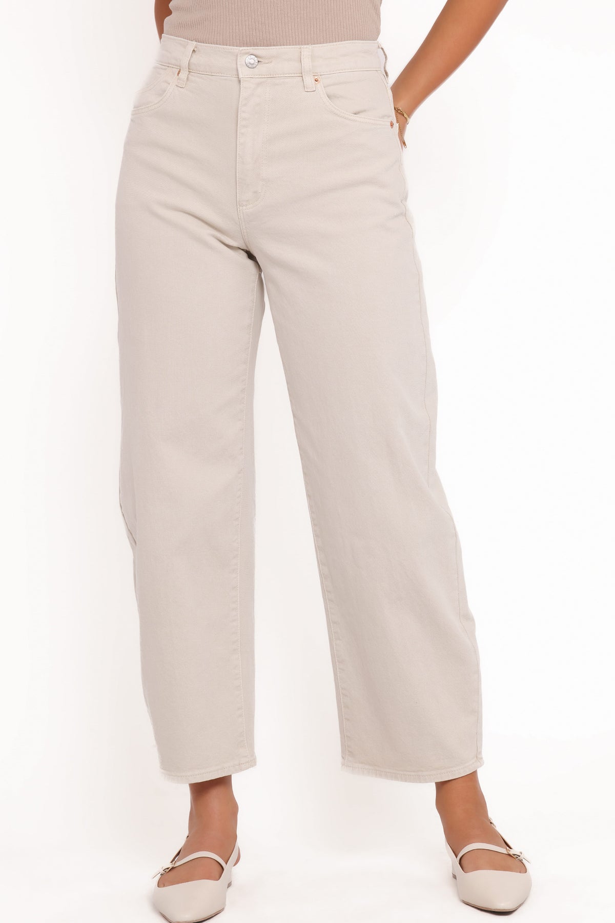 Close-up front view of off-white high-rise barrel jeans showing the waistband, silver button closure, belt loops, front scoop pockets and wide legs paired with beige ballet flats.