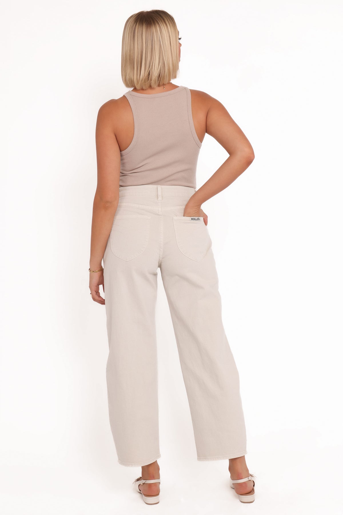 Rear view of off-white barrel jeans showing the high-rise waistband, curved yoke, signature spade-shaped back pockets and relaxed legs, styled with a beige sleeveless top and strappy heels.