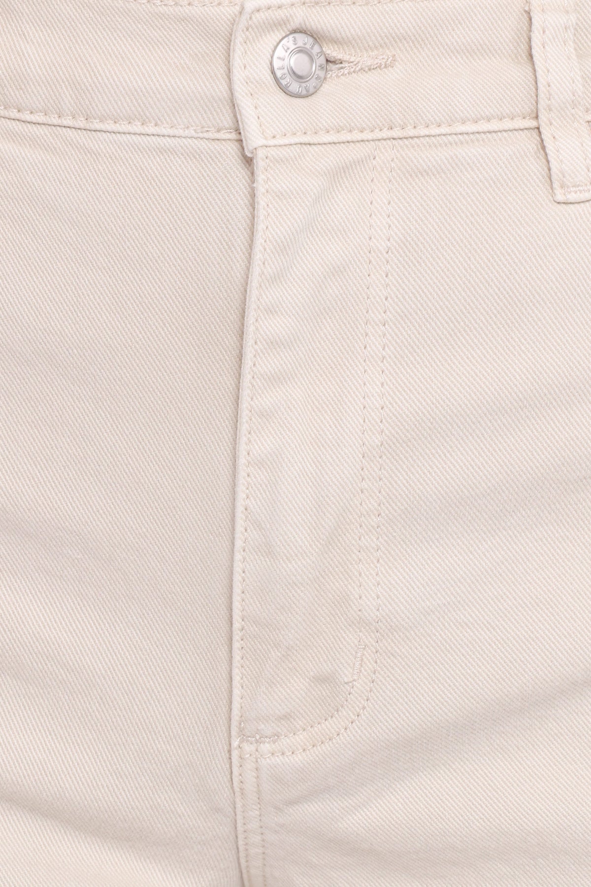 Close-up front detail of off-white denim showing the silver button, zip-fly closure, belt loop, stitching and curved edge of the front scoop pocket.