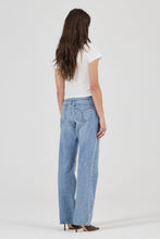 Person wearing light blue jeans and a white top on a plain background