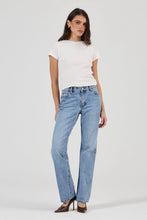 Woman wearing a white t-shirt and light blue jeans on a plain background