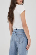 Person wearing a white t-shirt and light blue jeans on a plain background
