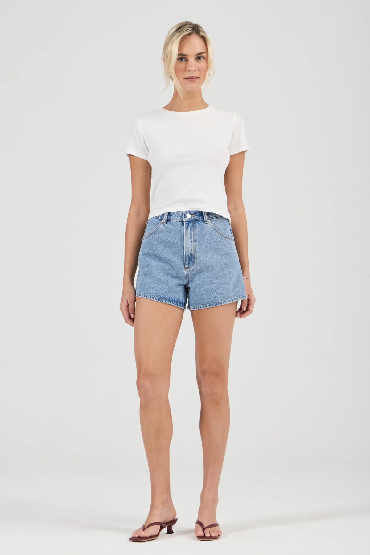 A close front view of mid-blue denim shorts showing the button fastening, belt loops, front pockets and contrasting seams.