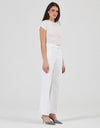 A model wearing vintage white high-rise jeans with a wide, flared leg, a fitted white short-sleeve tee and pointed-toe heels, shown from a three-quarter front angle to highlight the full-length silhouette.