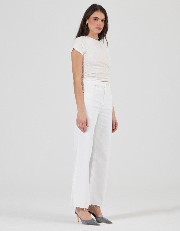 A model wearing vintage white high-rise jeans with a wide, flared leg, a fitted white short-sleeve tee and pointed-toe heels, shown from a three-quarter front angle to highlight the full-length silhouette.