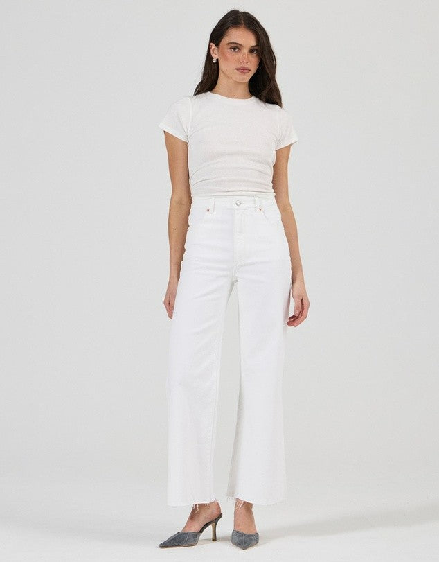 A model standing front-facing in vintage white high-rise jeans with a fitted white tee and grey pointed-toe heels, showing the waistband, front pockets and wide-leg cut.