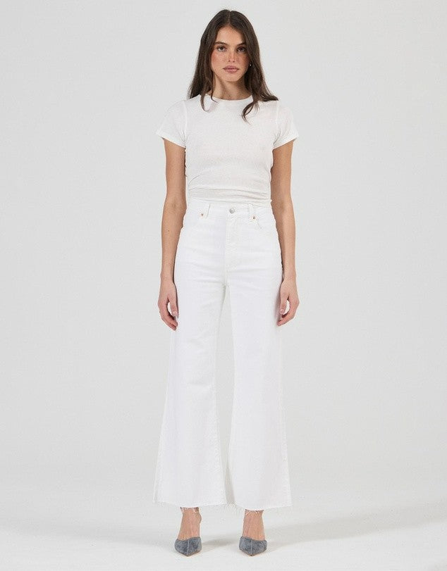 Full-length front view of vintage white jeans styled with a fitted white tee and grey heels, highlighting the flared hems and clean, monochromatic outfit.