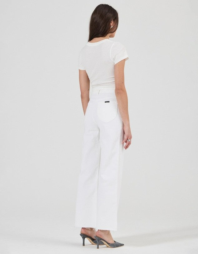 Rear three-quarter view of vintage white high-rise jeans worn with a fitted white tee and pointed-toe heels, showing the back pockets, waistband and full-length legs.