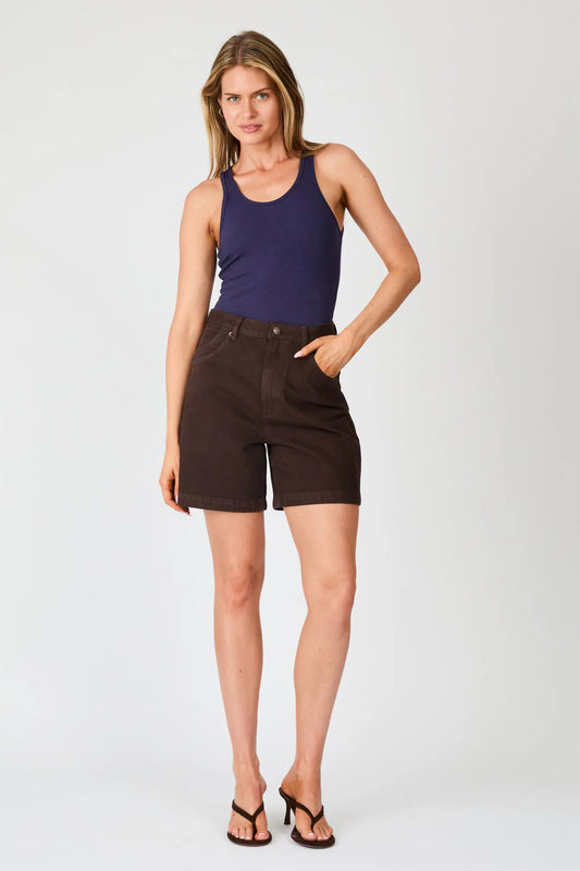 A full-length front view of chocolate brown high-rise denim shorts styled with a navy tank top and black heeled sandals.