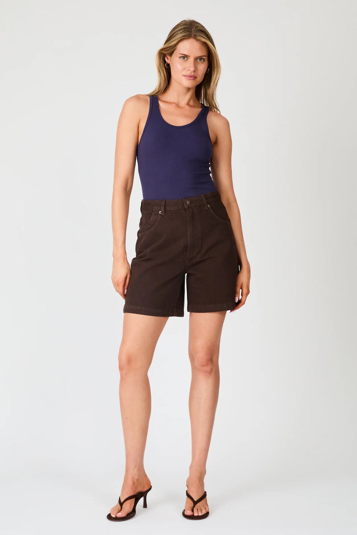 A front view of chocolate brown denim shorts showing the high-rise waist, button fastening, front scoop pockets and mid-thigh length.