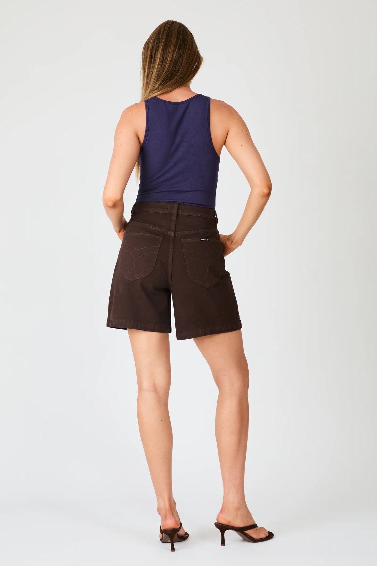 A rear view of chocolate brown denim shorts featuring two shaped back pockets, tonal stitching and a waistband.