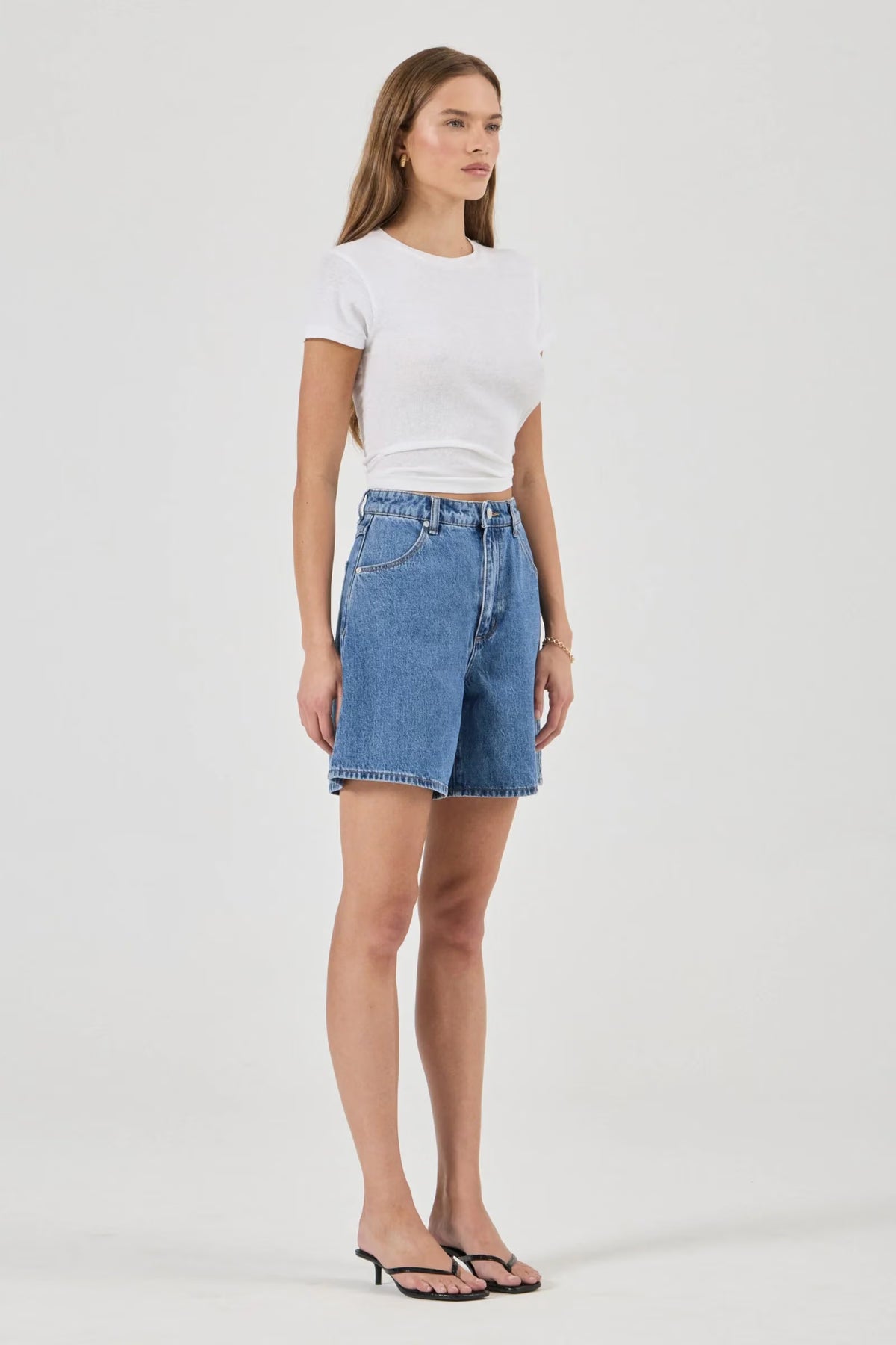Blue denim shorts shown from a three-quarter side view, highlighting the high-rise waist, scoop pocket and relaxed silhouette.