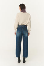 Person wearing blue jeans and a beige sweater on a white background