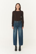 Woman wearing a brown long-sleeve top and blue jeans on a white background