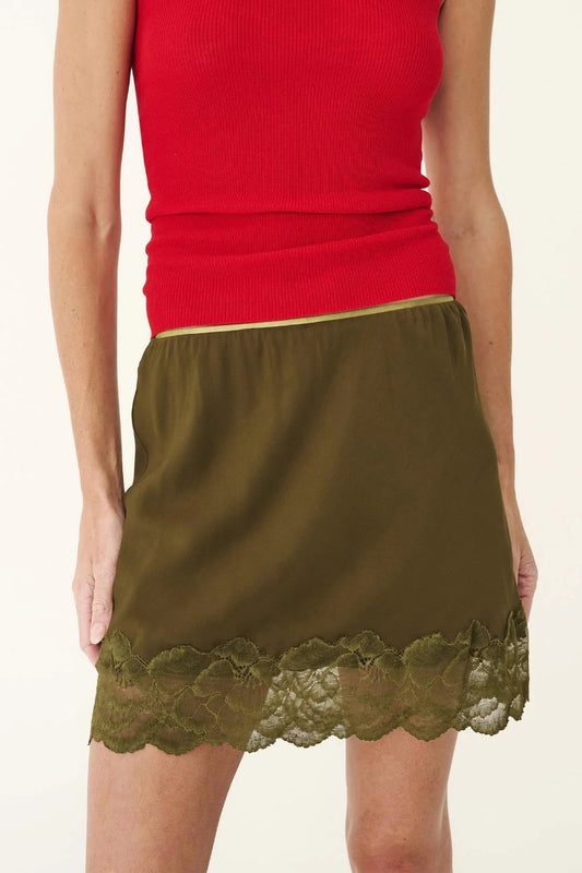 A model wearing a ribbed red tank top and an olive green mini skirt with a scalloped lace hem, shown against a plain off-white background.