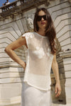A woman wears a bone crochet top with an open-weave design and floral motifs outdoors.
