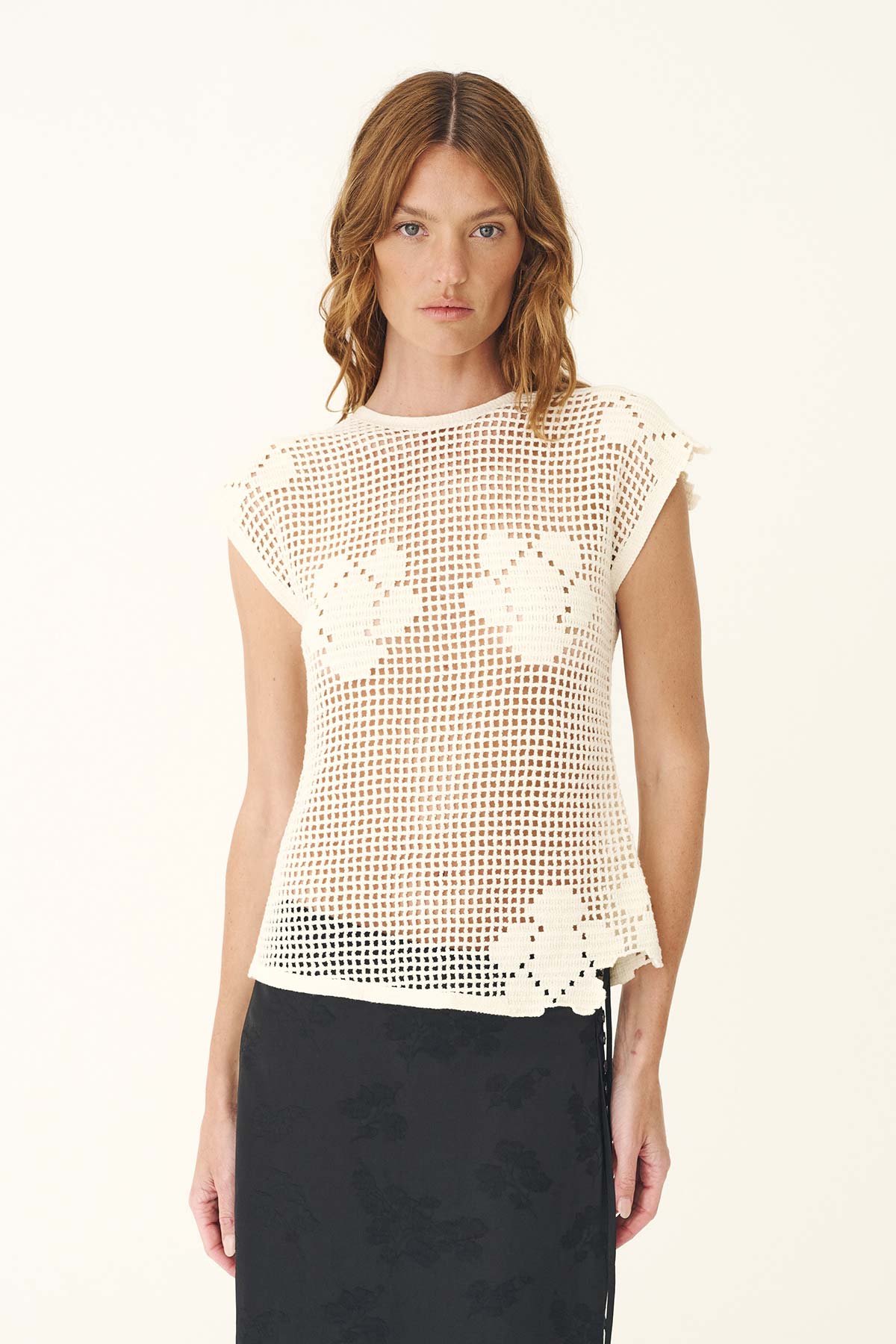 A woman wears a bone crochet top with floral motifs and a dark midi skirt in a front view.
