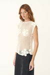 A woman wears the bone crochet top with a dark skirt in an angled side view.

