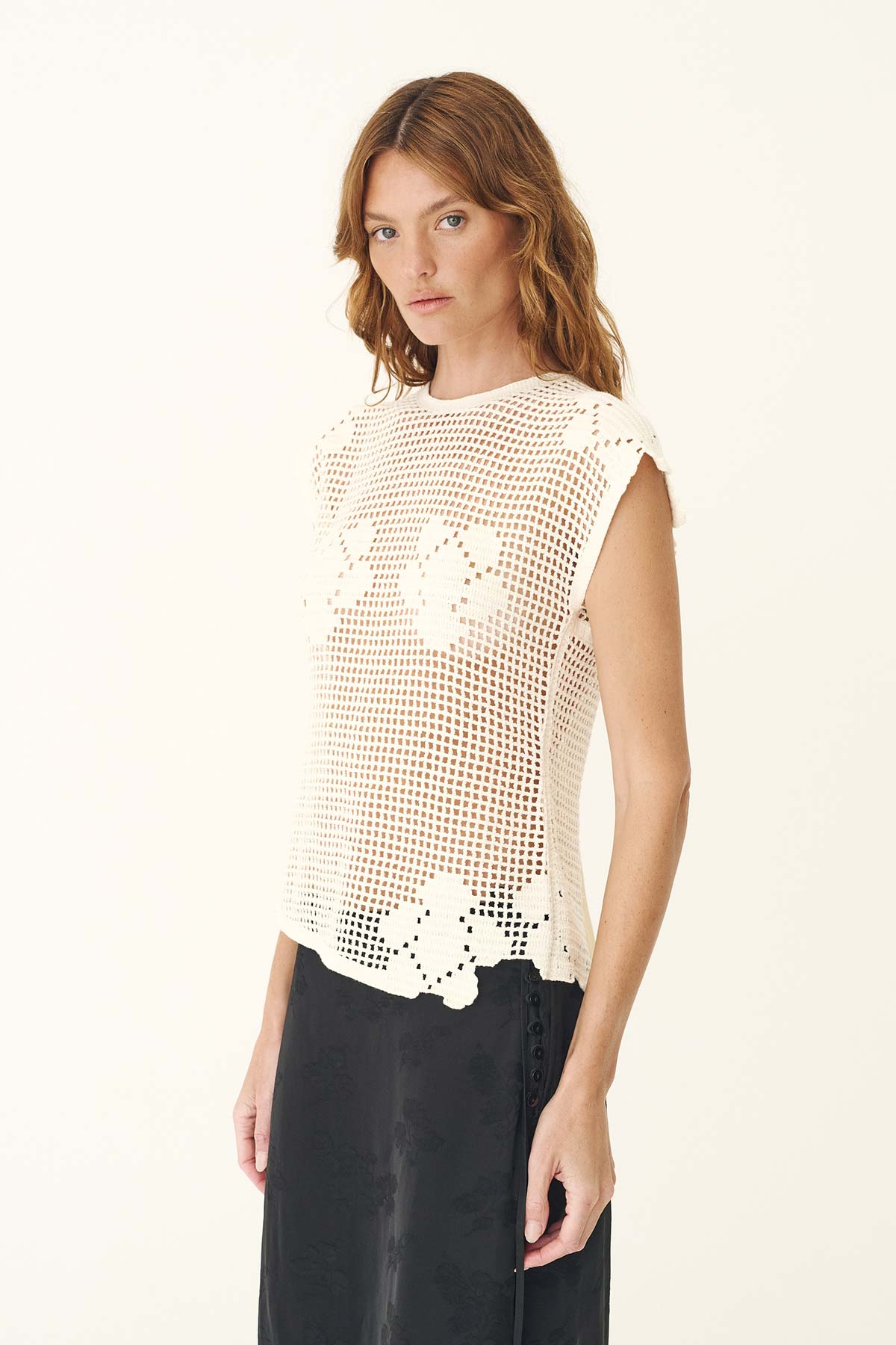 A woman wears the bone crochet top with a dark skirt in an angled side view.
