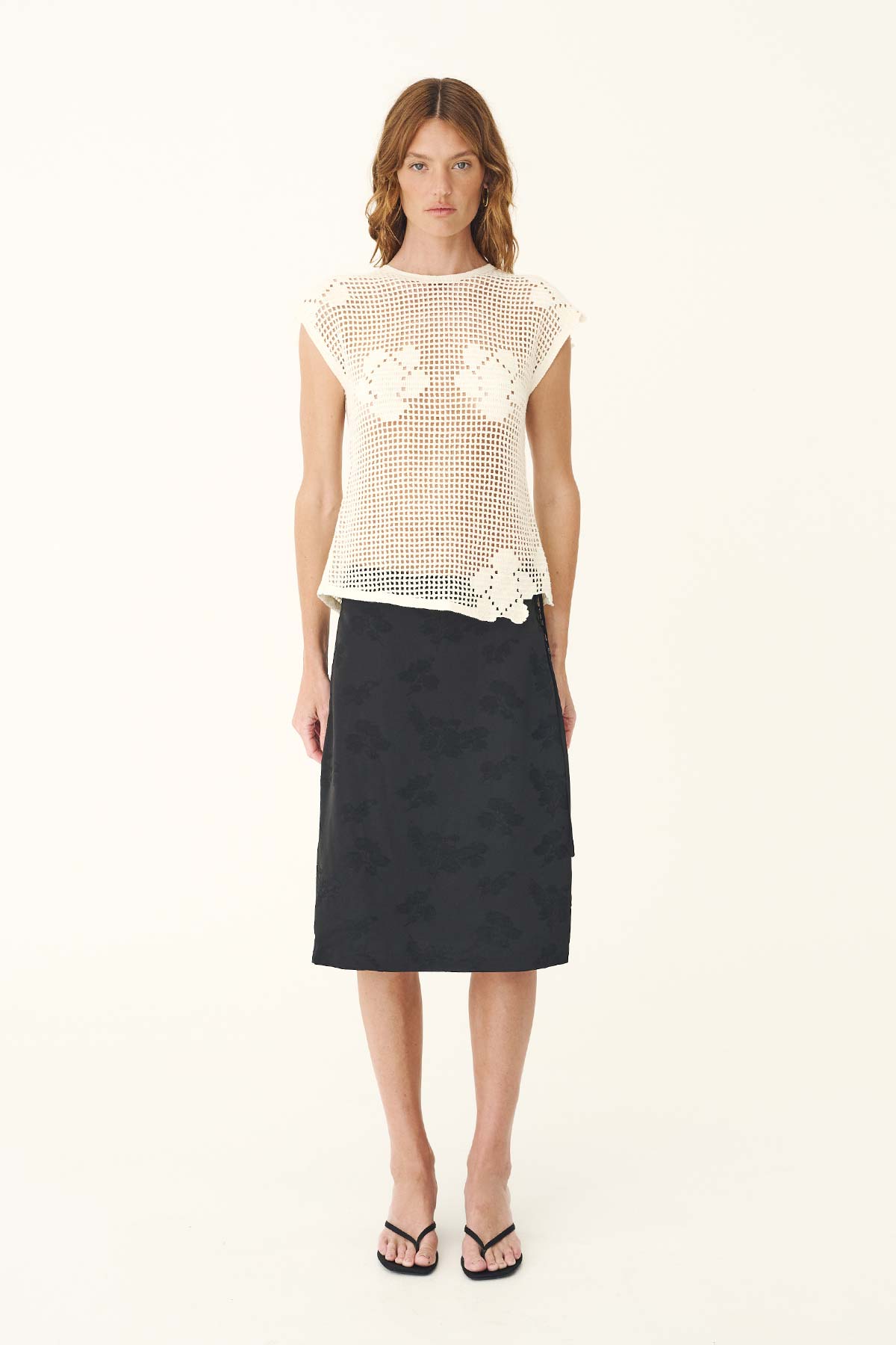 A woman wears the bone crochet top with a dark midi skirt in a full-length front view.
