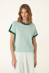 A woman wears a pale green short-sleeve knit tee with dark green contrast trim and a white skirt.
