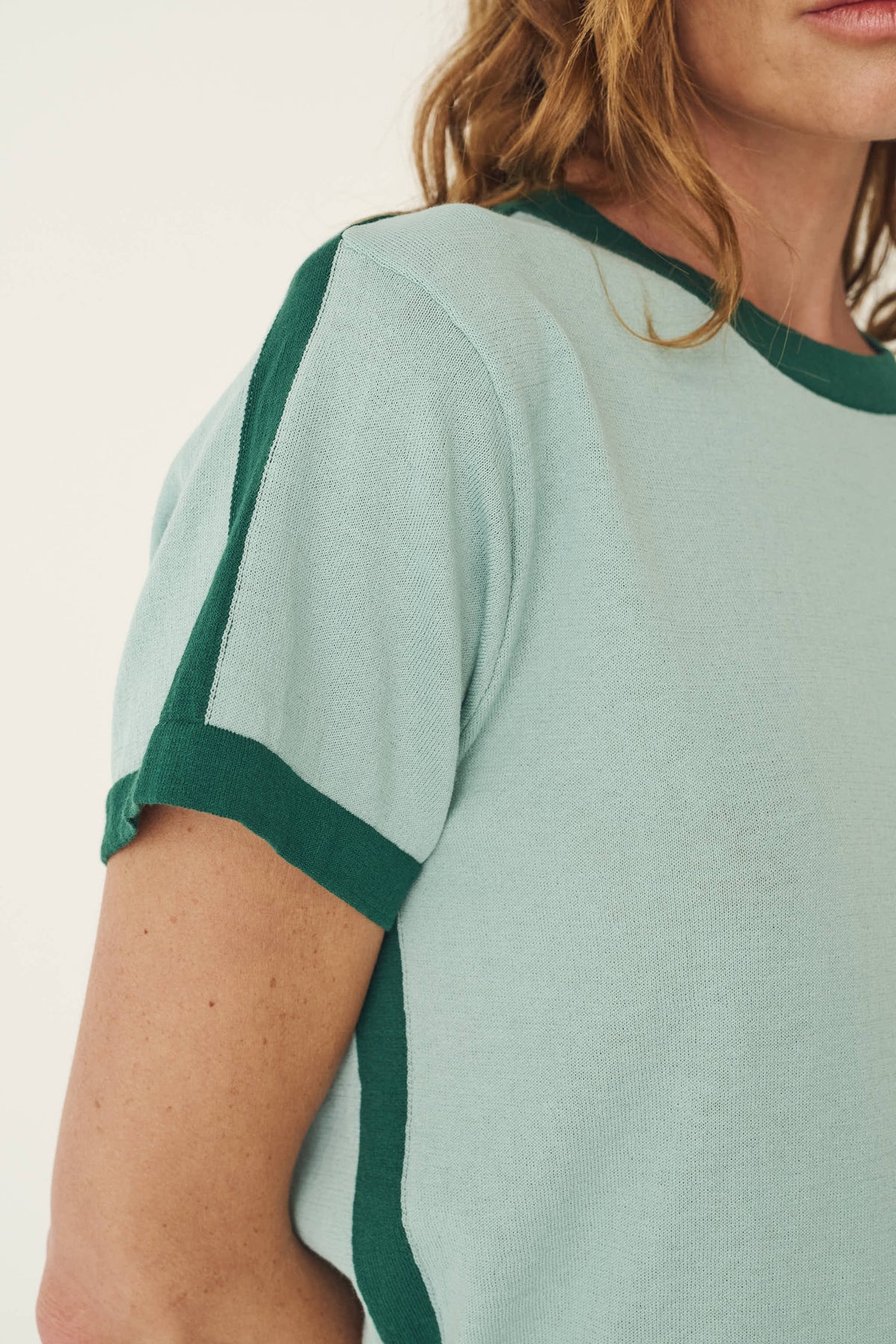 A close-up shows the pale green knit fabric with dark green contrast trim along the shoulder, sleeve and neckline.
