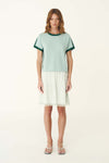 A woman wears the pale green short-sleeve knit tee with a white skirt in a full-length front view.