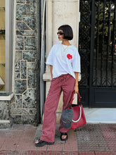 Woman in white shirt and red pants with a red bag standing on a sidewalk.