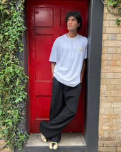 Person wearing a white t-shirt and black pants standing in front of a red door.