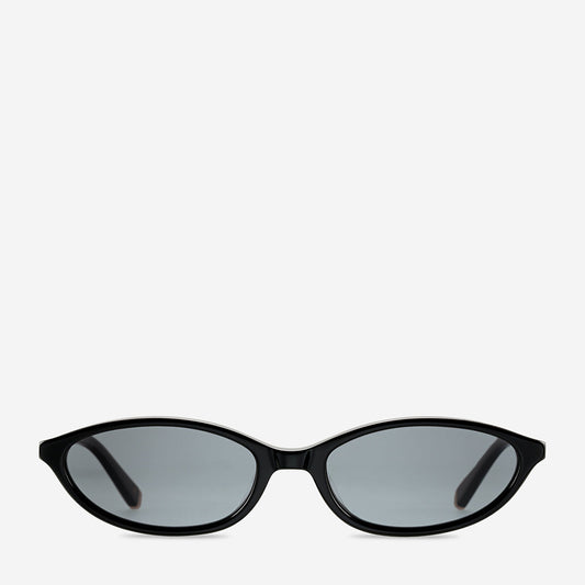 Black sunglasses shown from the front, featuring a slim curved frame, softly angled oval lenses, dark tinted lenses and subtle gold metal detailing at the outer edges.