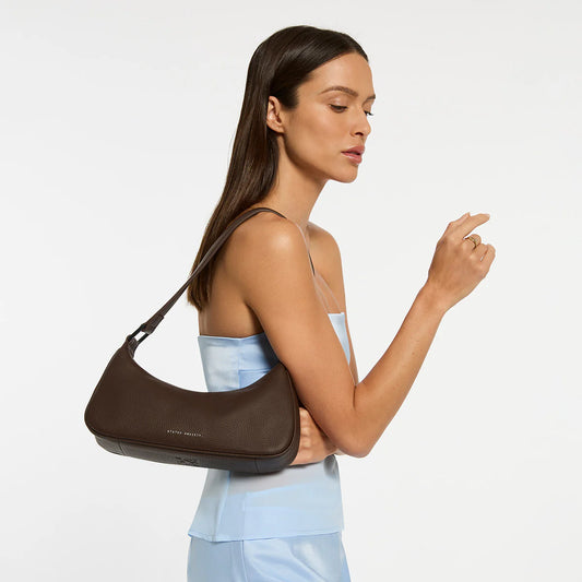 Woman carrying a brown shoulder bag on a plain background