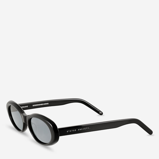 Black oval sunglasses shown from a three-quarter front angle, highlighting the curved frame and grey-tinted lenses.