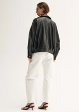 Person wearing a black leather jacket and white pants on a plain background