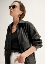 Person wearing a black leather jacket and sunglasses on a plain background