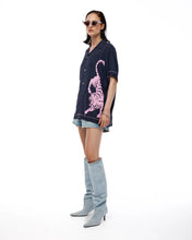 Woman wearing a dark blue oversized shirt with a pink tiger design, denim shorts, and gray knee-high boots on a white background.