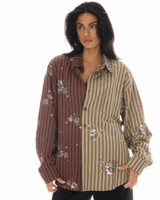 A model wears an oversized brown and beige striped shirt with floral sequin embellishments in a front close-up view.
