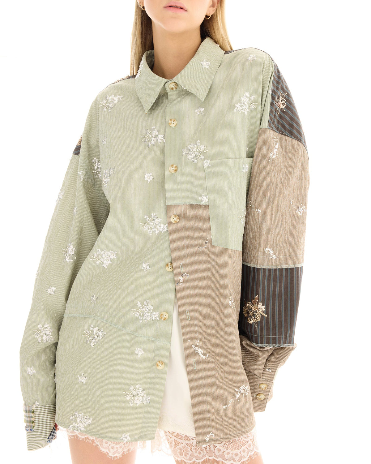 Close-up of the sage green patchwork shirt showing the pointed collar, tortoiseshell buttons, floral embellishments, contrast panels and chest pocket.