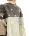 Close-up back view showing the shirt's charcoal pinstripe, sage green and taupe patchwork panels with scattered floral embellishments and a denim back yoke patch.
