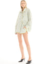 A woman wearing sage and white striped runner shorts with pastel floral embellishments, styled with a matching oversized shirt and black heeled mules.