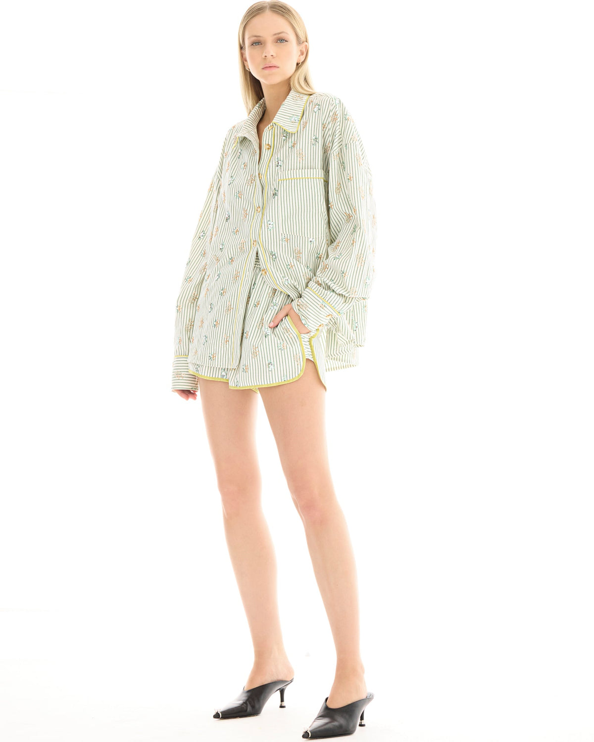 A woman wearing sage and white striped runner shorts with pastel floral embellishments, styled with a matching oversized shirt and black heeled mules.