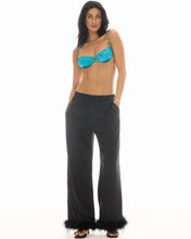 A model wears black wide-leg floral pants with feather-trimmed hems in a full-length front studio view.
