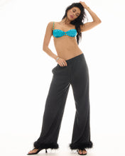A model wears the black feather-trim pants in an angled front view with a turquoise top and heeled sandals.
