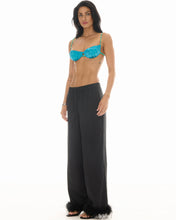 A model wears the black wide-leg floral pants in a side studio view showing the relaxed silhouette and feather hems.
