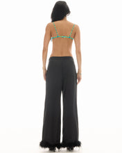 A model wears the black feather-trim pants in a back studio view showing the full-length wide-leg fit.
