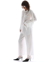 A model wears the white lace-hem floral pants with a matching oversized shirt in an angled side view.
